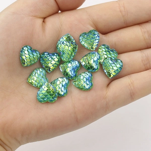 Macro shot of green heart-shaped resin fish scale cabochons held in palm for DIY crafts