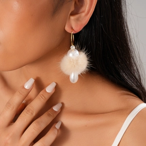 Close-up of golden C-shape earrings with beige pompom and faux pearl drop on model