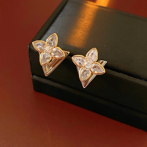 Macro detail of gold and silver four-leaf clover stud earrings with clear zircon stones