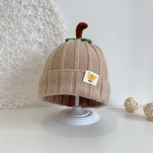Detail of beige knit baby hat with pumpkin leaf top and small cartoon baby patch
