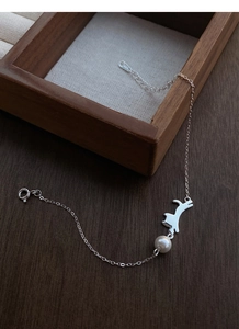 Dettaglio del bracciale gatto in argento S925 con perla bianca su fondo legno