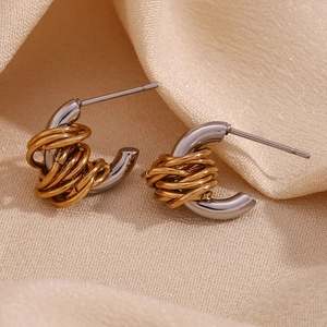 Macro shot of two-tone C-shape stainless steel earrings with gold wire wrap on beige fabric