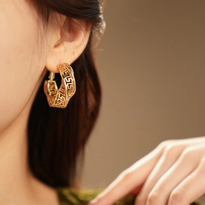 Macro shot of gold hollow twisted hoop earrings with engraved Greek Key patterns