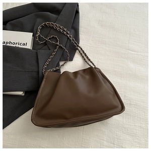 Top view of a brown pleated cloud bag with a metal chain strap on beige fabric