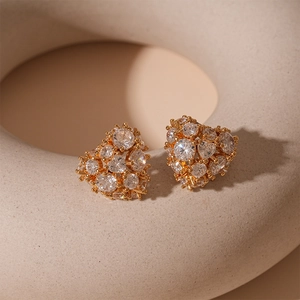 Detailed view of heart-shaped gold studs with sparkling cubic zirconia on a soft pedestal