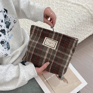 Detailed shot of brown plaid tweed pouch featuring a white fabric label and zipper closure