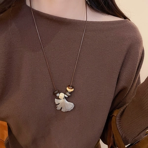 Close-up of a silver ginkgo leaf pendant with beaded ethnic cord on model neck