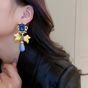 Close-up of vintage gold earrings with blue gemstones and bow detail on a model
