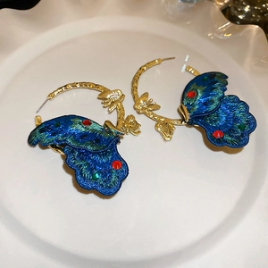 Detailed close-up of blue embroidered butterfly wings on vintage gold textured hoop earrings