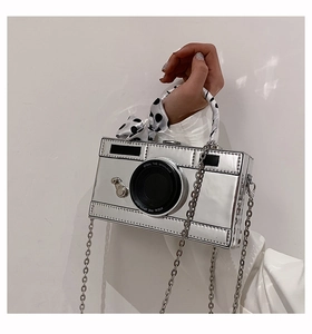 Detailed shot of creative silver camera-shaped handbag with silk scarf handle and metal chain