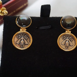 Close-up of vintage gold coin earrings with bee motifs and dark grey pearls on black velvet