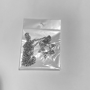 Detail view of hexagram star pendant necklace in transparent packaging on a grey surface