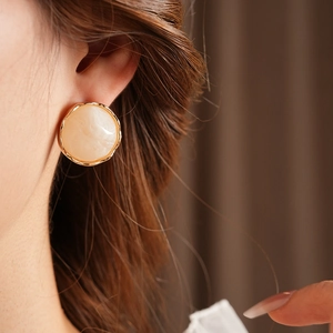 Close-up of vintage round gold earrings with beige marble texture worn by a model