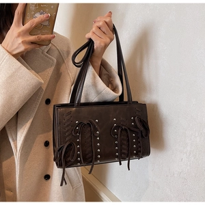 Detailed close-up of dark brown PU leather handbag with silver rivets and bow accent