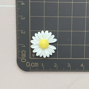 2cm white resin daisy flower charm with yellow center on a metric measuring mat