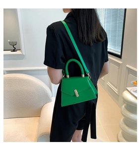 Modern green trapezoid handbag with gold clasp worn as a shoulder bag by a model