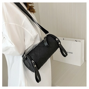 Close-up of black cylinder crossbody bag with textured fabric and wide strap