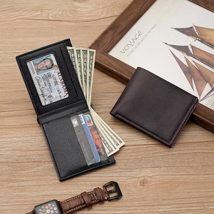 Short bifold leather wallet for men in black and dark brown on a wooden desk with a watch