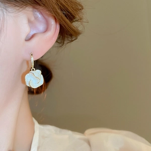 Macro view of gold-plated camellia flower earrings with zircon detailing on female model