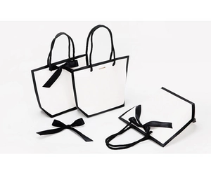Detail of white shopping bags with black trim, rope handles, and elegant ribbon bows