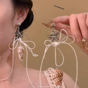 Detail view of starfish silver stud earrings with shell pendants and white bow tie