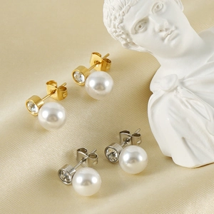 Dettaglio degli orecchini a perno con perle e strass su elegante tessuto di seta champagne