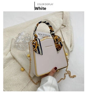 Detailed view of a white box bag with gold metal frame and silk scarf wrapped handle