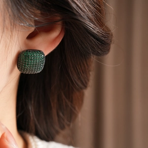 Close-up of vintage square emerald zircon stud earrings with black metal worn on ear