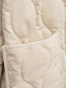 Detail of beige quilted cotton jacket featuring woven trim and precision stitching