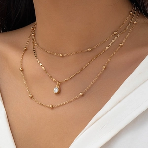 Close-up of layered gold necklace set with rhinestone pendant and beaded chain links