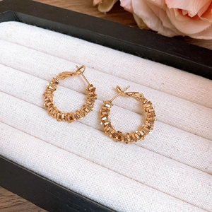 Detail of golden geometric hoop earrings with woven texture on a velvet jewelry display