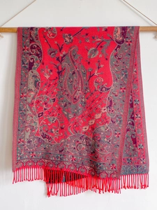 Detail of red paisley cashmere scarf with ethnic tassels hanging on a wooden rod