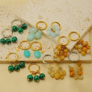 Detalle de aros dorados hechos a mano con cuentas de malaquita verde sobre una piedra