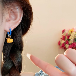 Close-up of yellow pumpkin charm earring on model with blue hoop and floral background