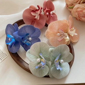 Detail of four colorful fabric orchid hair clips with pearls on a wooden tray