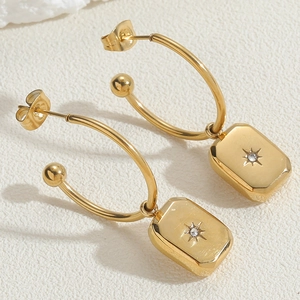Macro detail of gold-plated stainless steel hoop earrings with starburst pendant and zircon