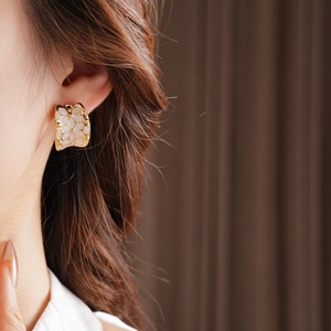Détail de boucles d'oreilles rétro dorées avec pétales en émail blanc sur mannequin femme