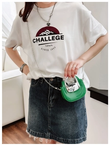 Close-up of green mini chain bag with silver metal handle worn as a crossbody by a model