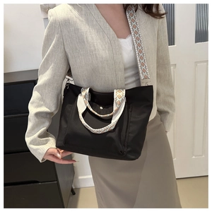 Nylon tote bag in black featuring colorful ethnic style woven strap worn by a model