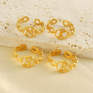 Detail of 18K gold letter rings M, K, S, R on beige stone and silk background