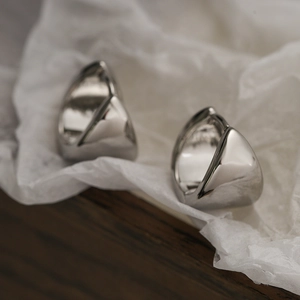 Minimalist silver triangular hoop earrings on elegant textured paper and dark wood