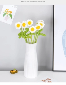 Close-up of hand-knitted white daisies with yellow centers in a white ceramic vase