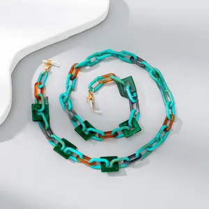 Detail of colorful acrylic chain links in teal and amber with golden lobster clasps