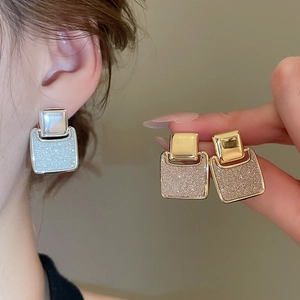 Close-up of geometric square earrings with 18k gold plating and shimmering glitter finish