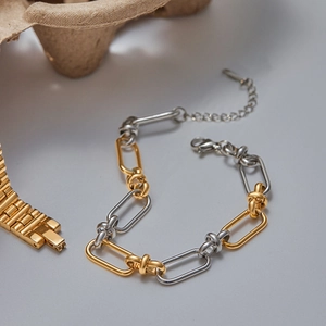 Detail of two-tone gold and silver chain bracelet with lobster clasp on a textured prop
