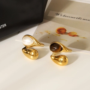 Detailed close-up of teardrop tiger eye and pearl stones set in gold stainless steel rings
