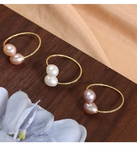 Detailed view of natural freshwater pearl rings with wavy gold bands on wooden surface