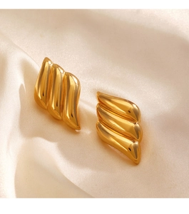 Macro shot of gold-plated flame-shaped stud earrings on beige silk fabric background