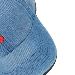 Macro detail of washed blue denim fabric and red embroidery on baseball cap side