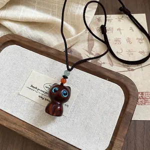 Handcrafted wooden cat pendant necklace with woven rope and blue eyes on a rustic background